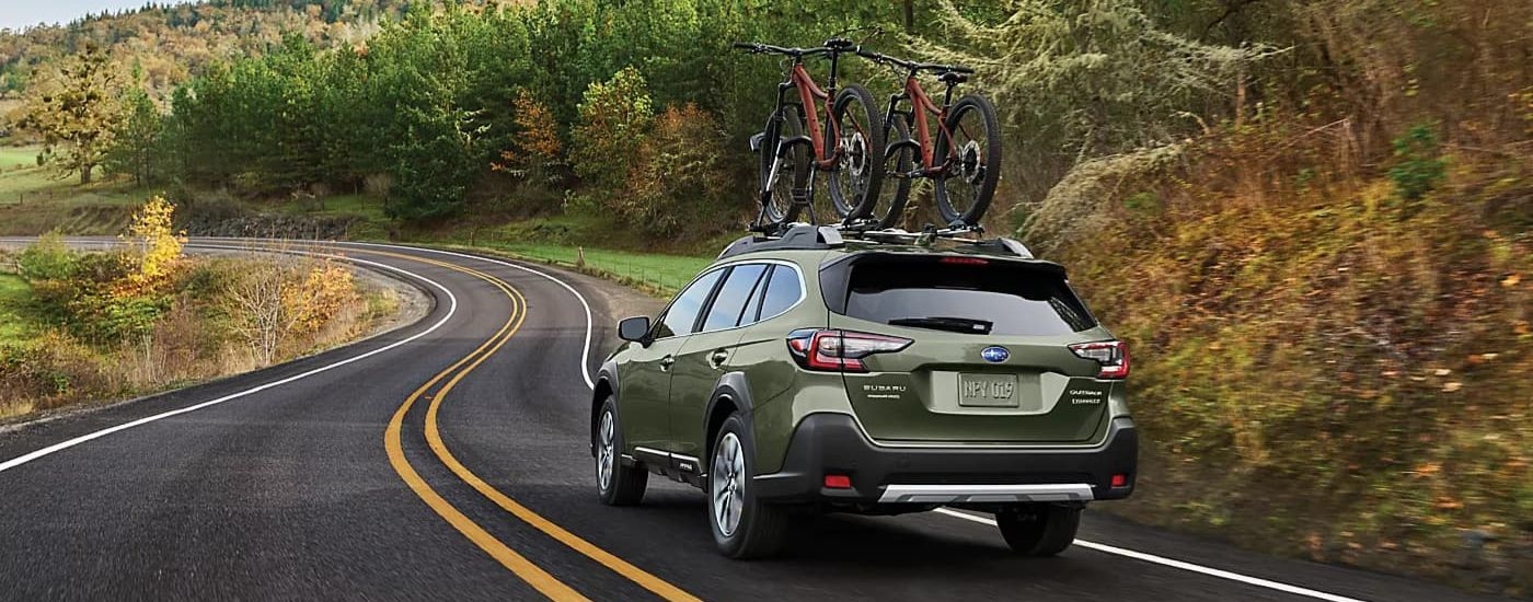 Green 2024 Subaru Outback driving on a winding road.
