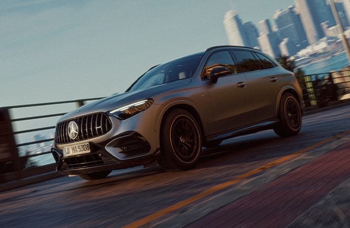2027 Mercedes-AMG GLC 53 SUV in matte gray driving past a city skyline, front three-quarter view