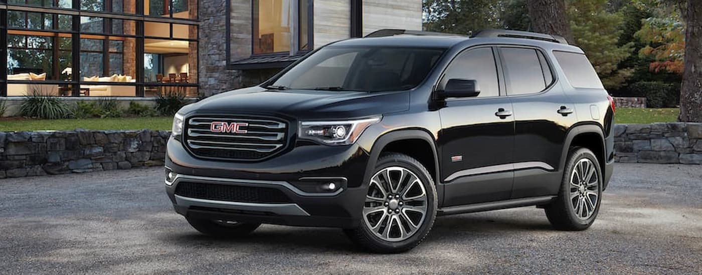 A black 2017 GMC Acadia is parked on a gravel driveway near a modern style home.