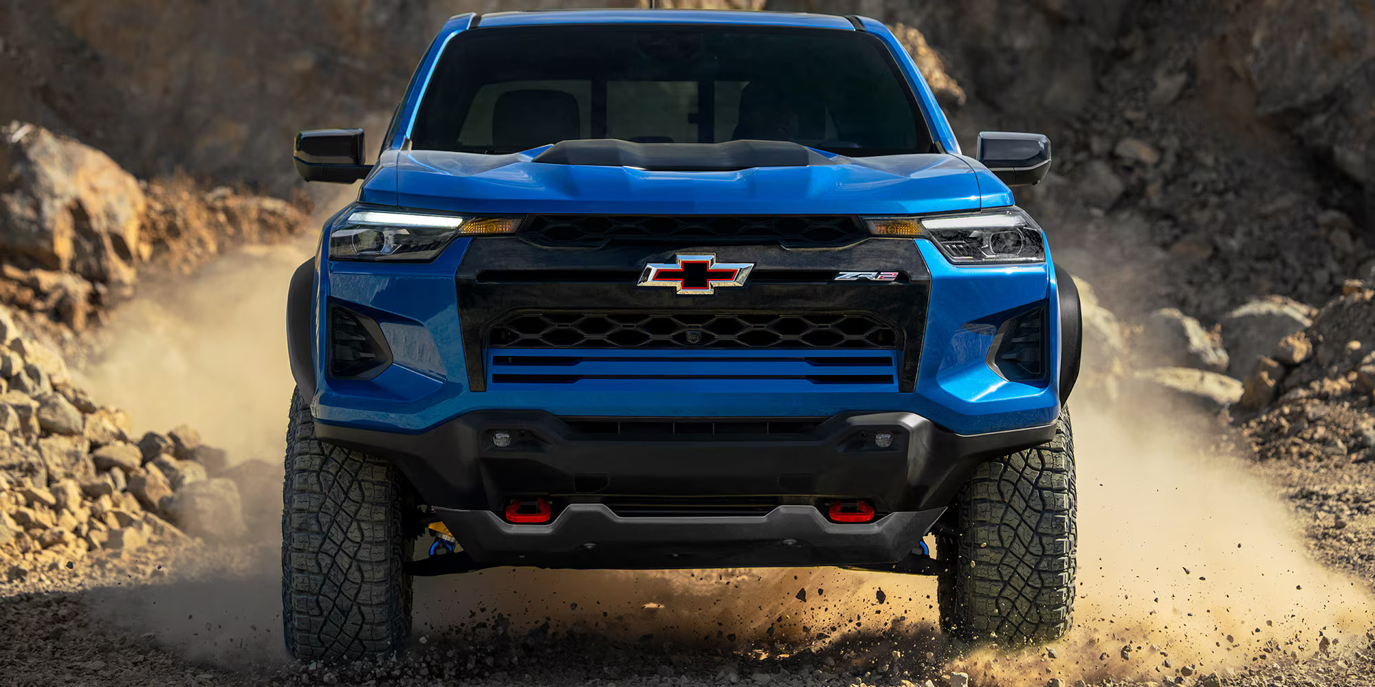 A blue chevrolet colorado driving on a dirt road.