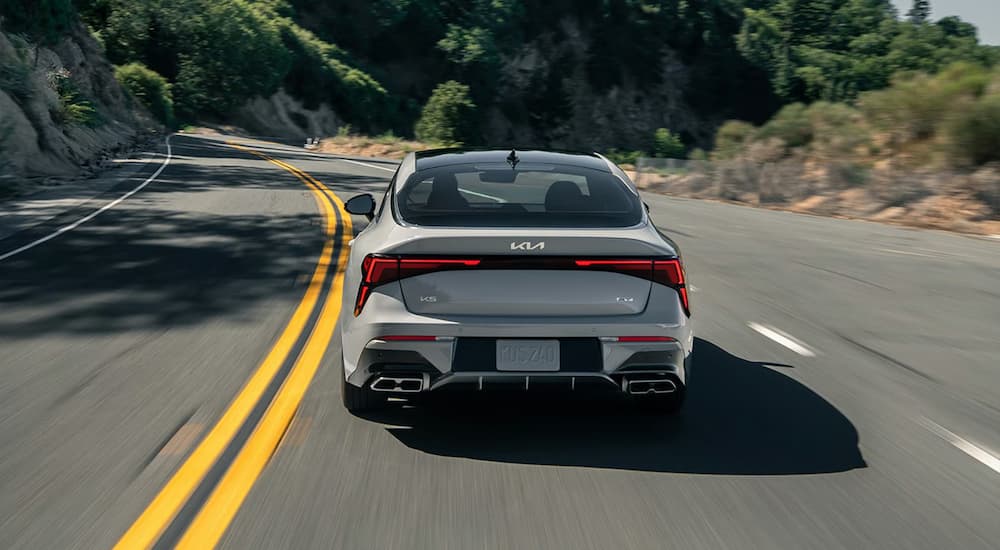 Rear of a grey 2026 Kia K5 for sale driving on a highway