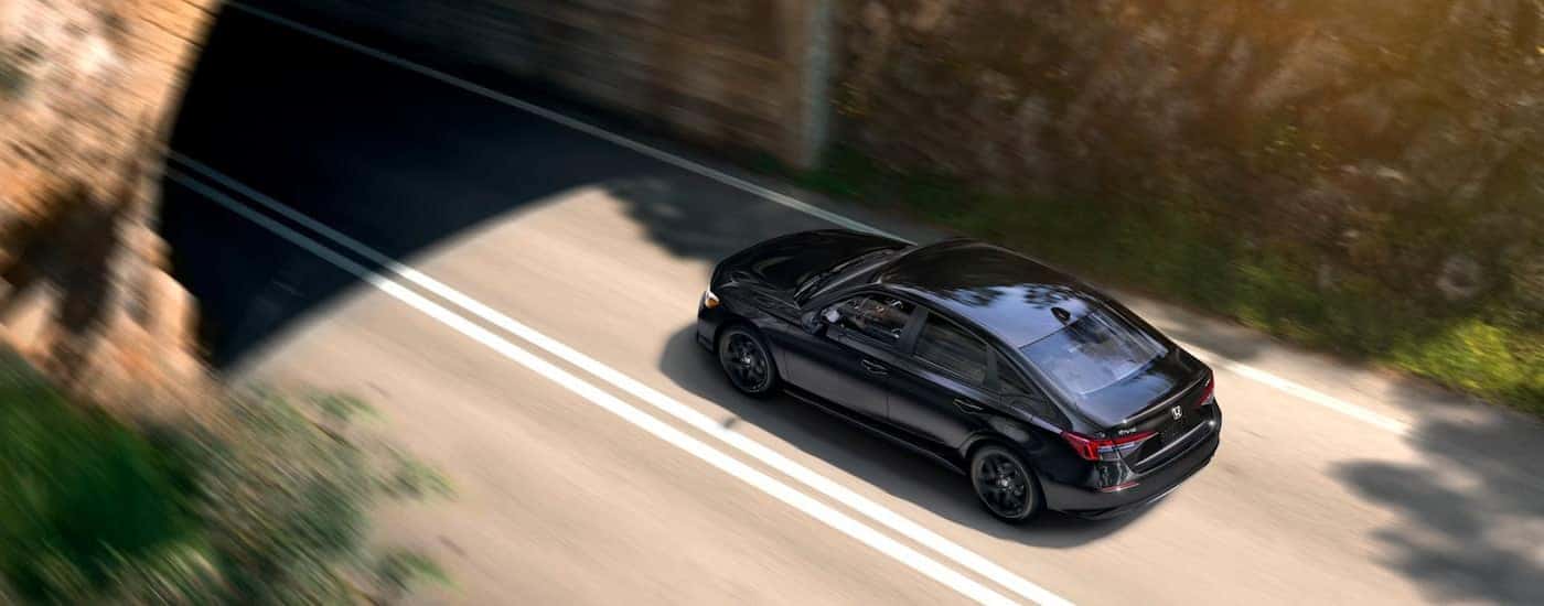 A black 2025 Honda Civic Sport is driving on a road to a tunnel.