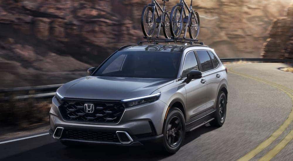 A silver 2023 Honda CR-V Sport Touring is shown driving on an open road.