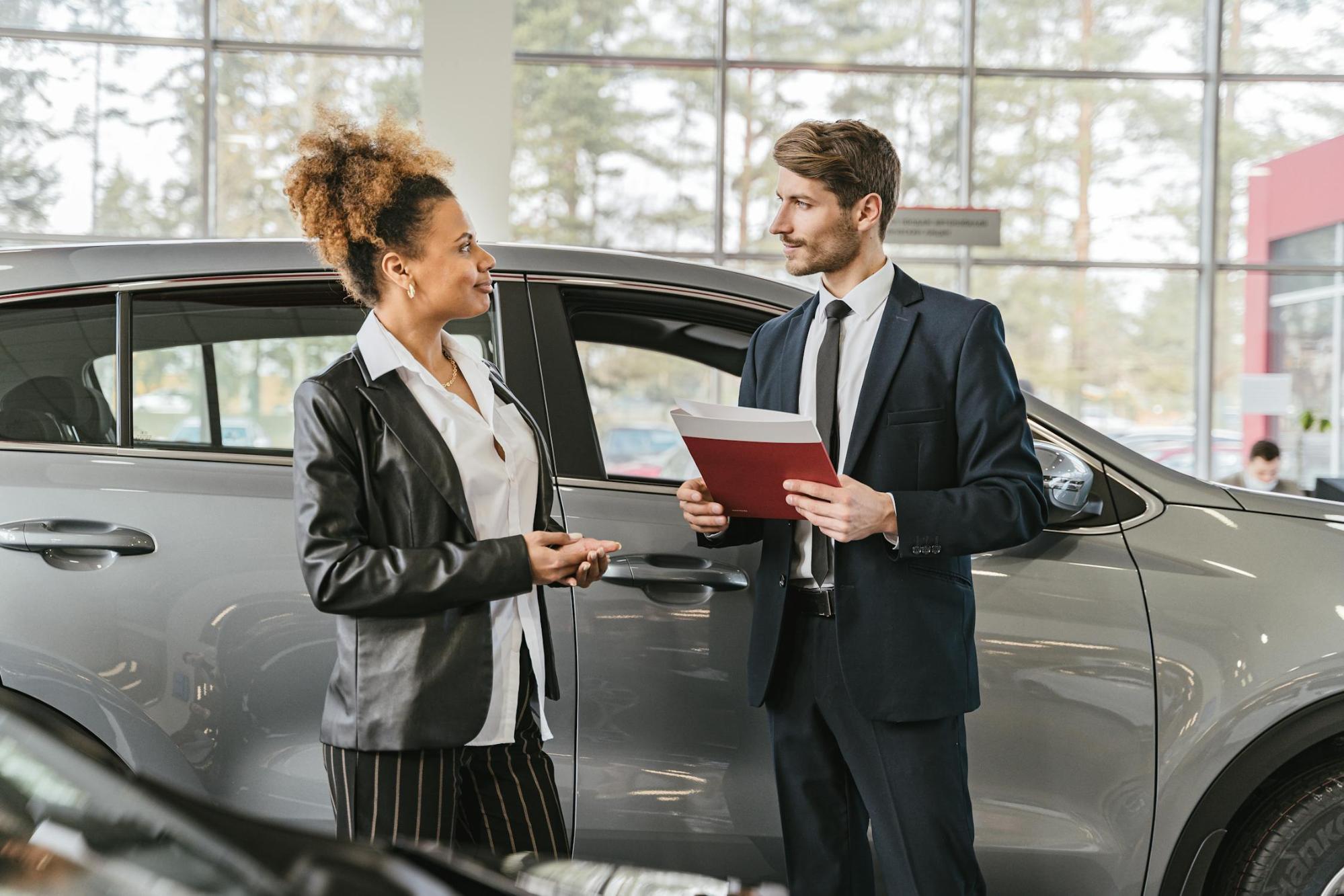  A woman talks with a car salesperson while standing next to a silver SUV inside a dealership showroom.