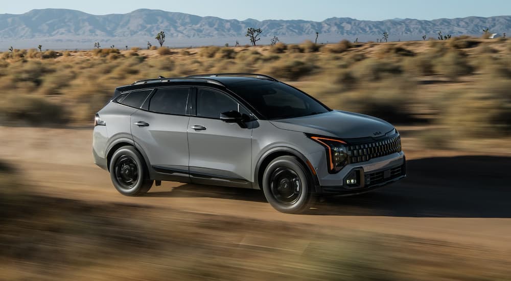 Grey 2026 Kia Sportage driving down a dirt road.