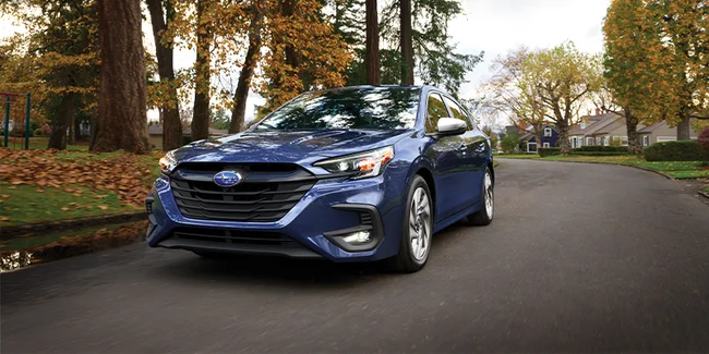Blue 2023 Subaru Legacy sedan on a tree-lined road