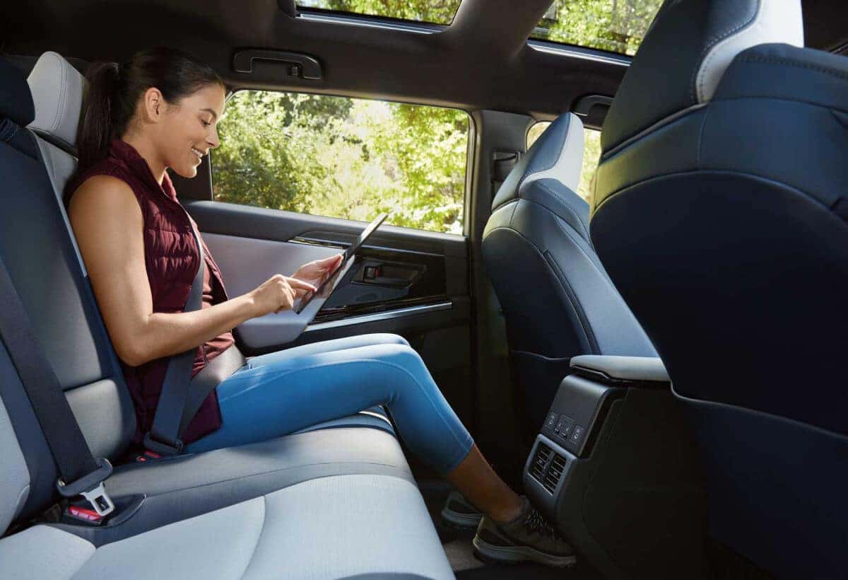 Woman relaxing in the spacious rear seat of a Subaru, using a tablet