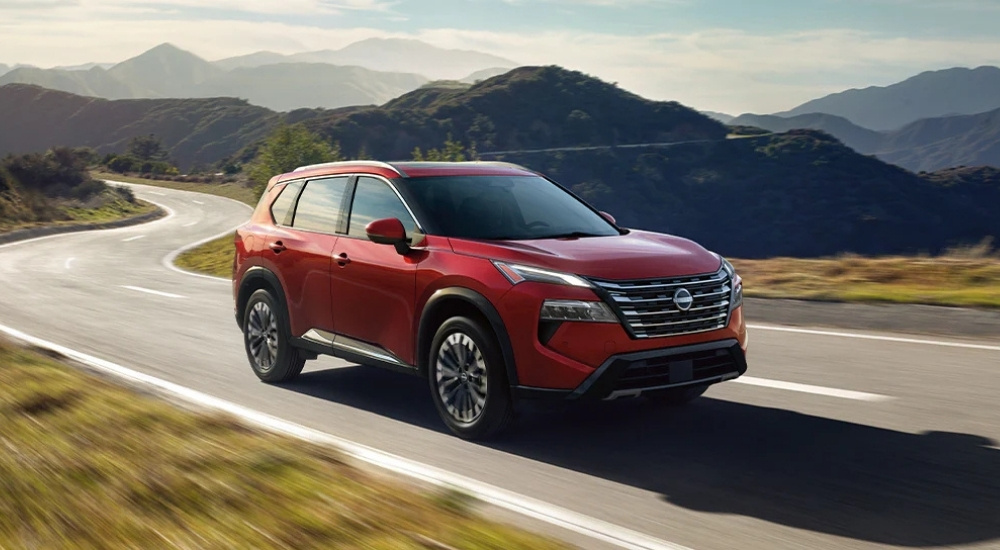 Red 2026 Nissan Rogue driving on a winding mountain road