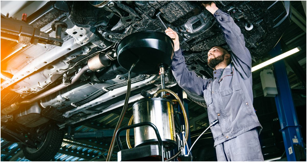 Subaru technician working beneath a vehicle on a lift during an oil change