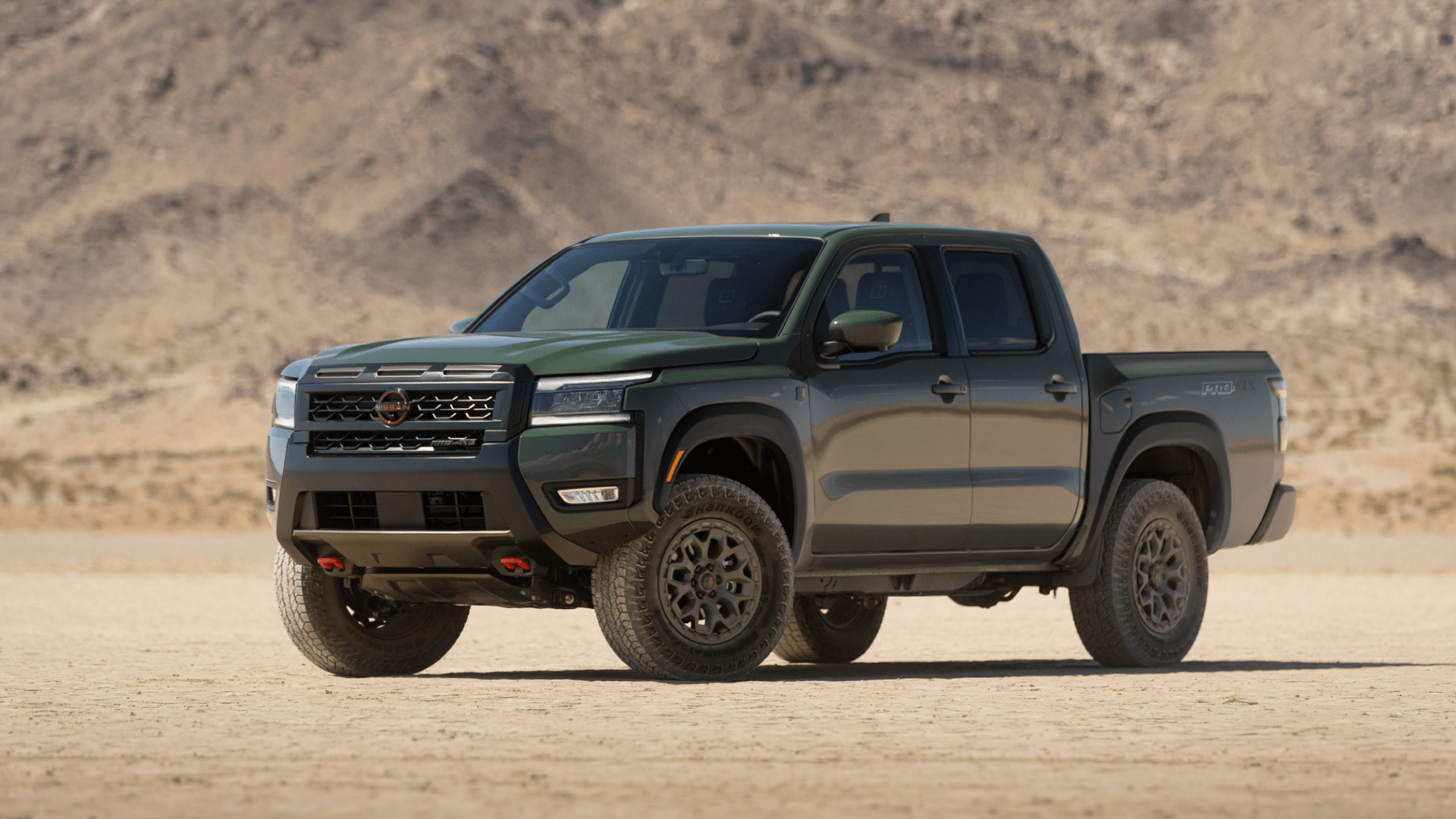 2026 Nissan Frontier® PRO-4X green pickup truck parked on desert terrain with rugged mountains behind.