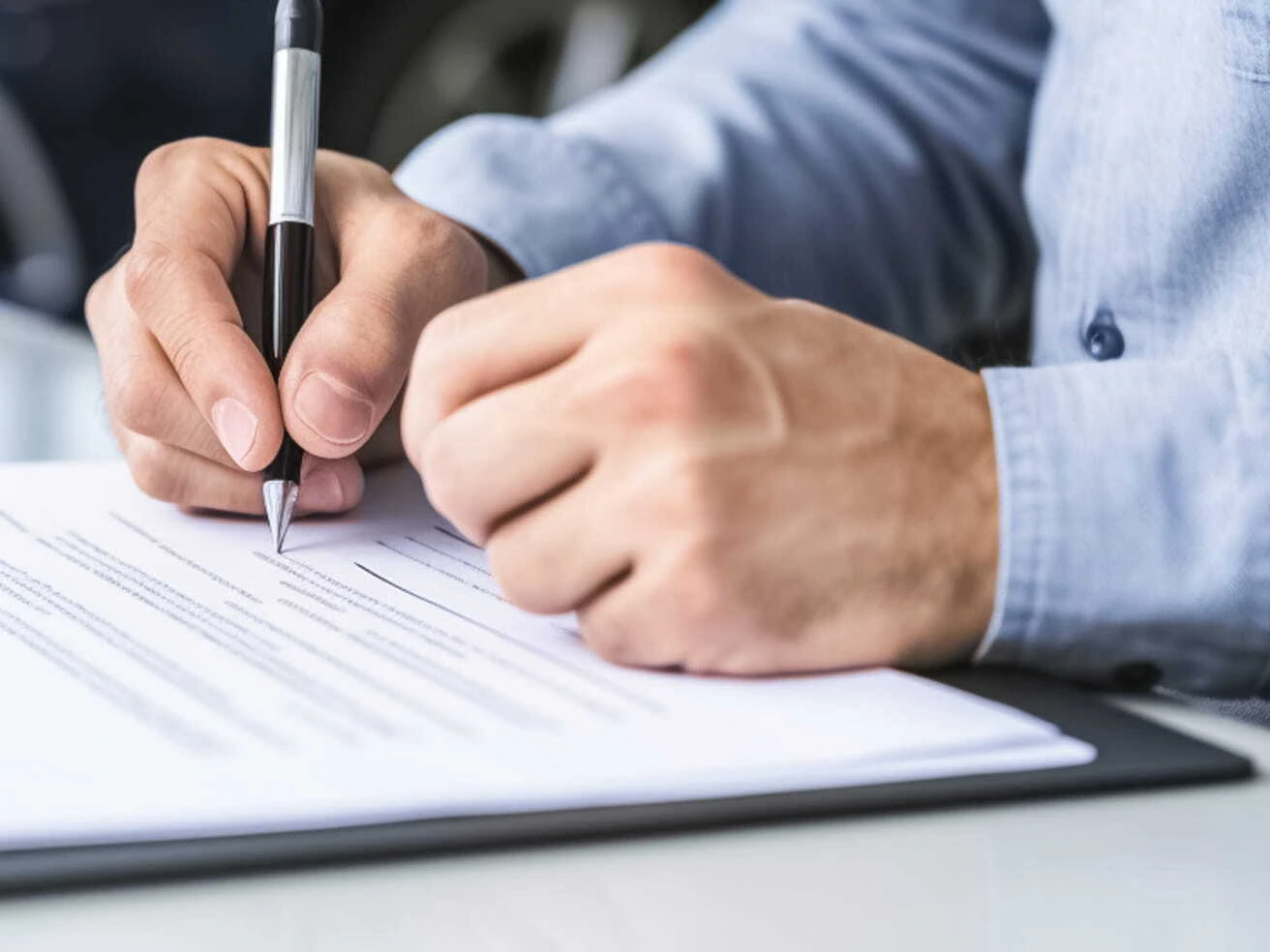 Close-up of a person signing paperwork with a pen on a desk.