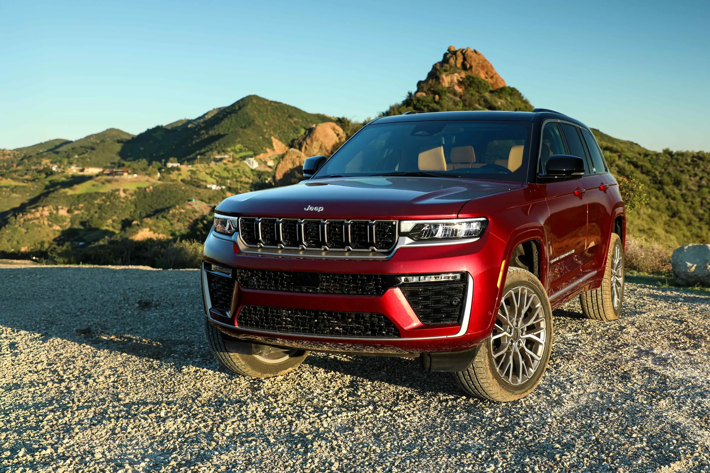 2026 Red Jeep Grand Cherokee parked on a gravel surface with a rocky mountain peak in the background