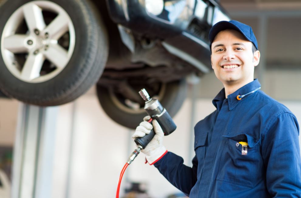 service tech smiles while holding a tool with car on lift in the background