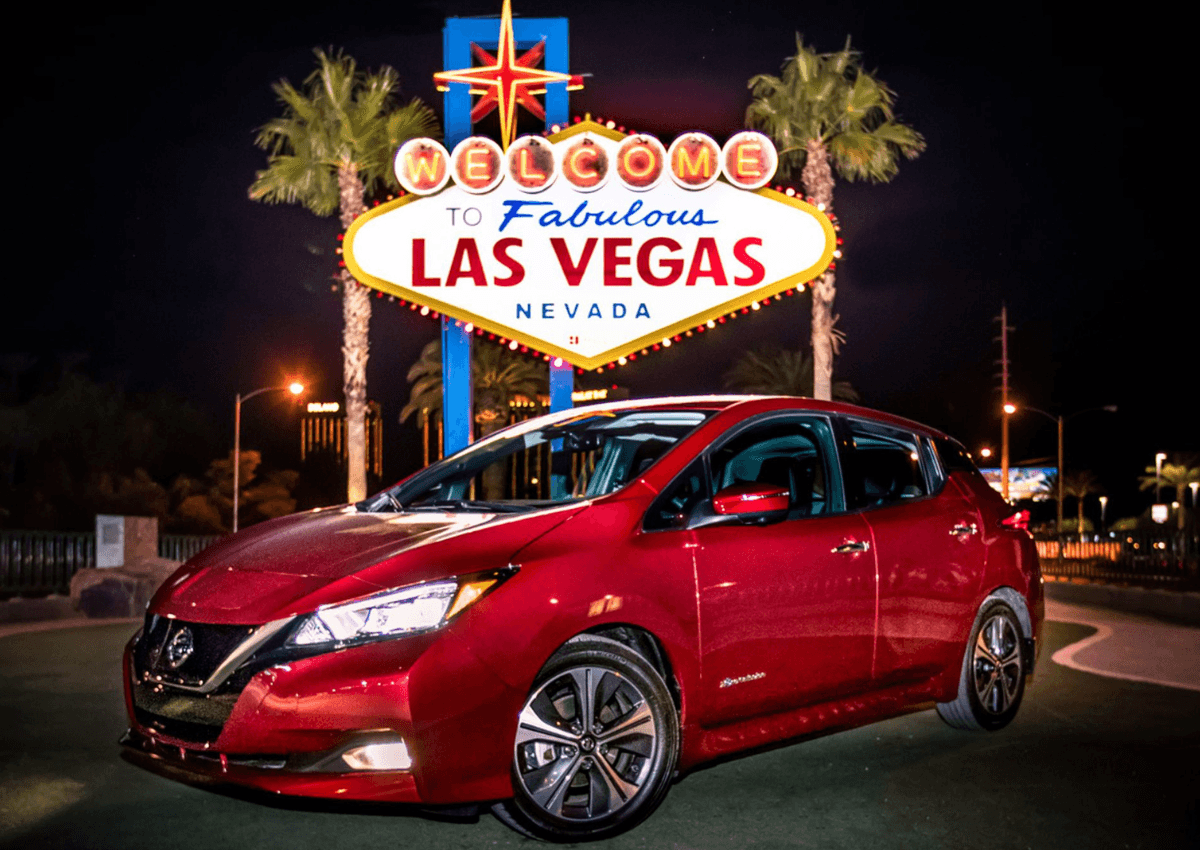 Red Nissan LEAF parked in front of the Welcome to Fabulous Las Vegas sign at night