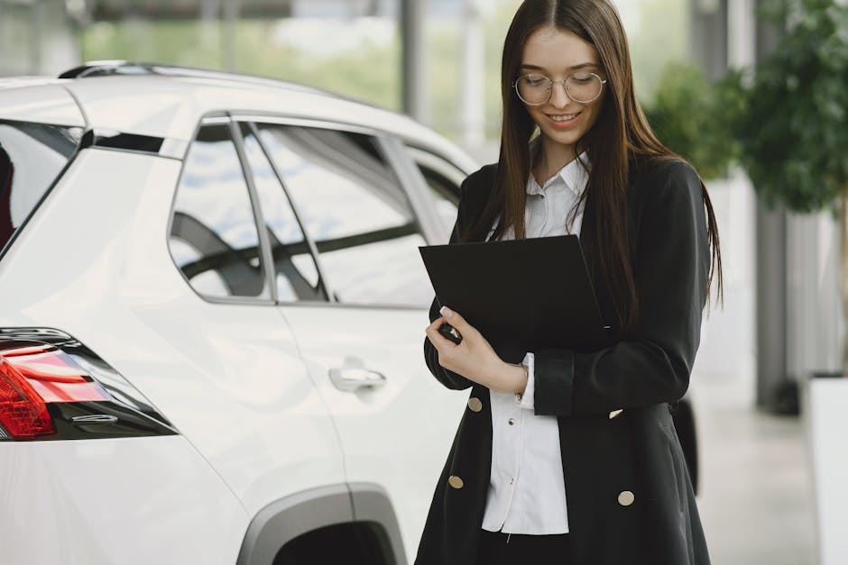 Smiling woman in a black jacket reviewing documents near a white car indoors.