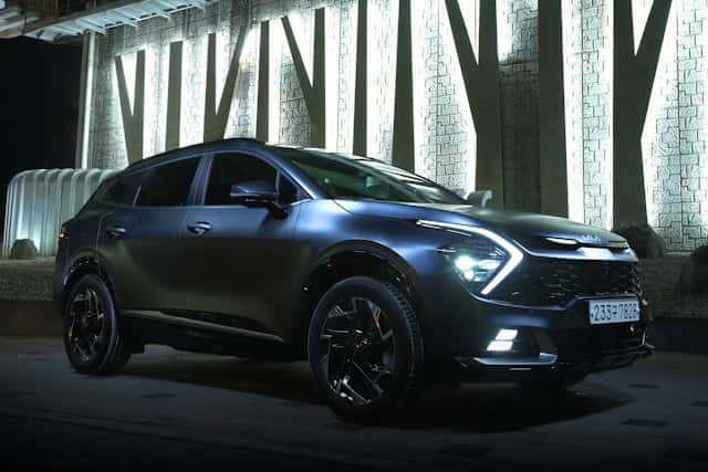 2026 Kia Sportage SUV in sleek black exterior, illuminated against a textured wall, showcasing modern design and advanced features for navigating wet Oregon roads.