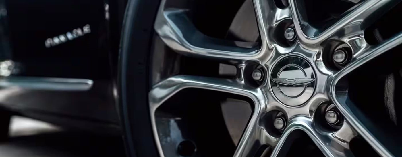 A close up shows a chrome rim on a black 2024 Chrysler Pacifica.