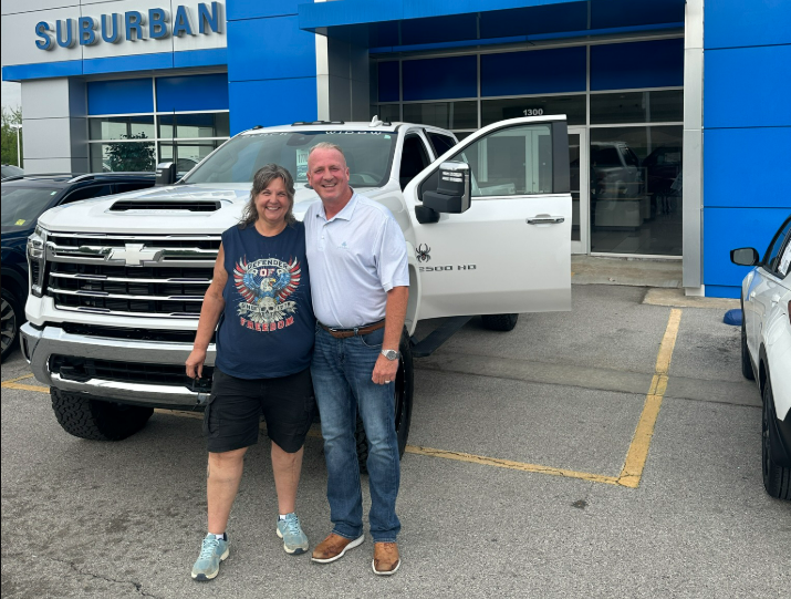 Woman smiling in front of a new chevrolet silverado 2500 hd in white with the sales agent who sold her the truck near Bixby, OK