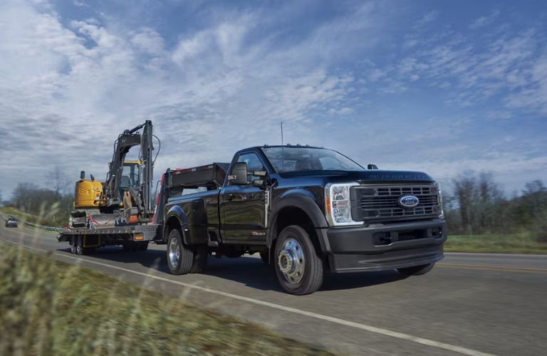 Black 2024 Ford Super Duty Towing a Backhoe on a Trailer