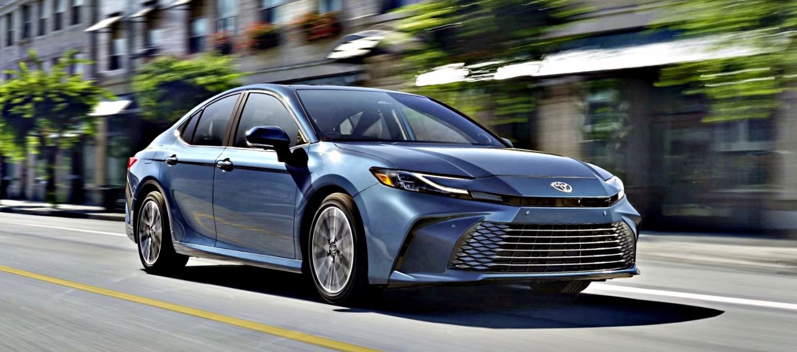 2025 Toyota Camry Hybrid driving on a city street, highlighting its modern design and blue exterior.