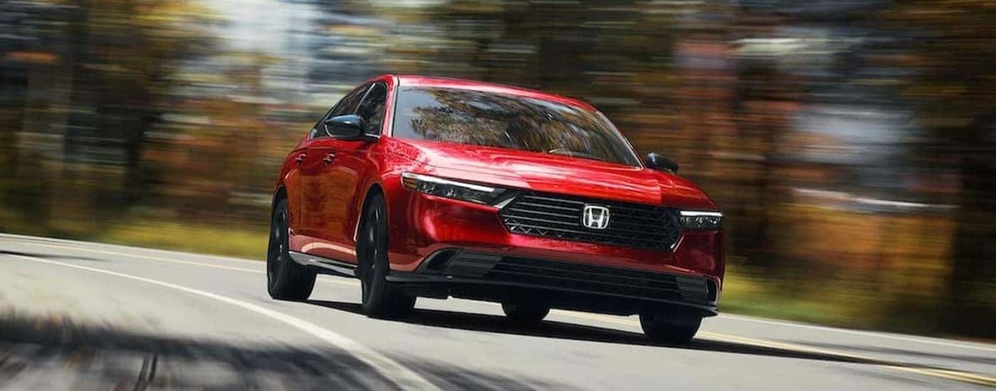 A popular Honda Accord Hybrid for sale, a red 2024 Honda Accord Sport-L Hybrid, is shown driving on a highway.
