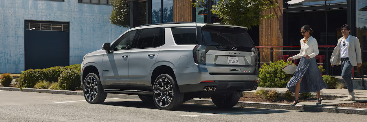 a silver chevrolet tahoe pakred next to a commercial building with a woman walking towards it