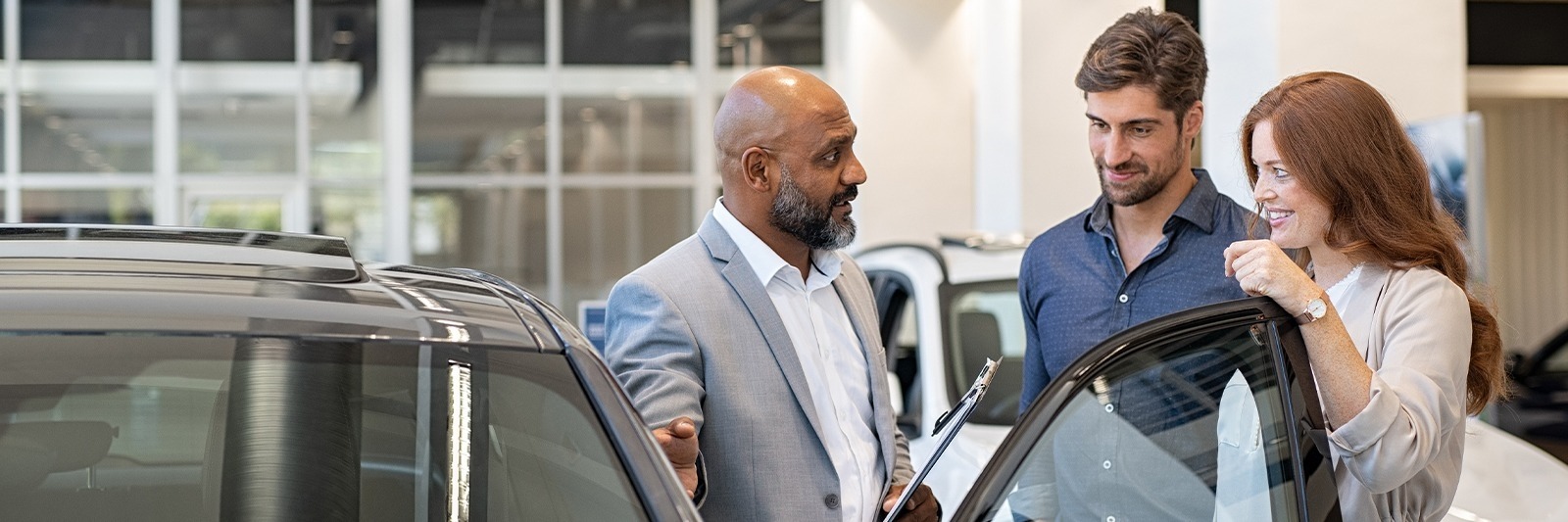Salesperson with a clipboard showing a new vehicle to a couple in the showroom