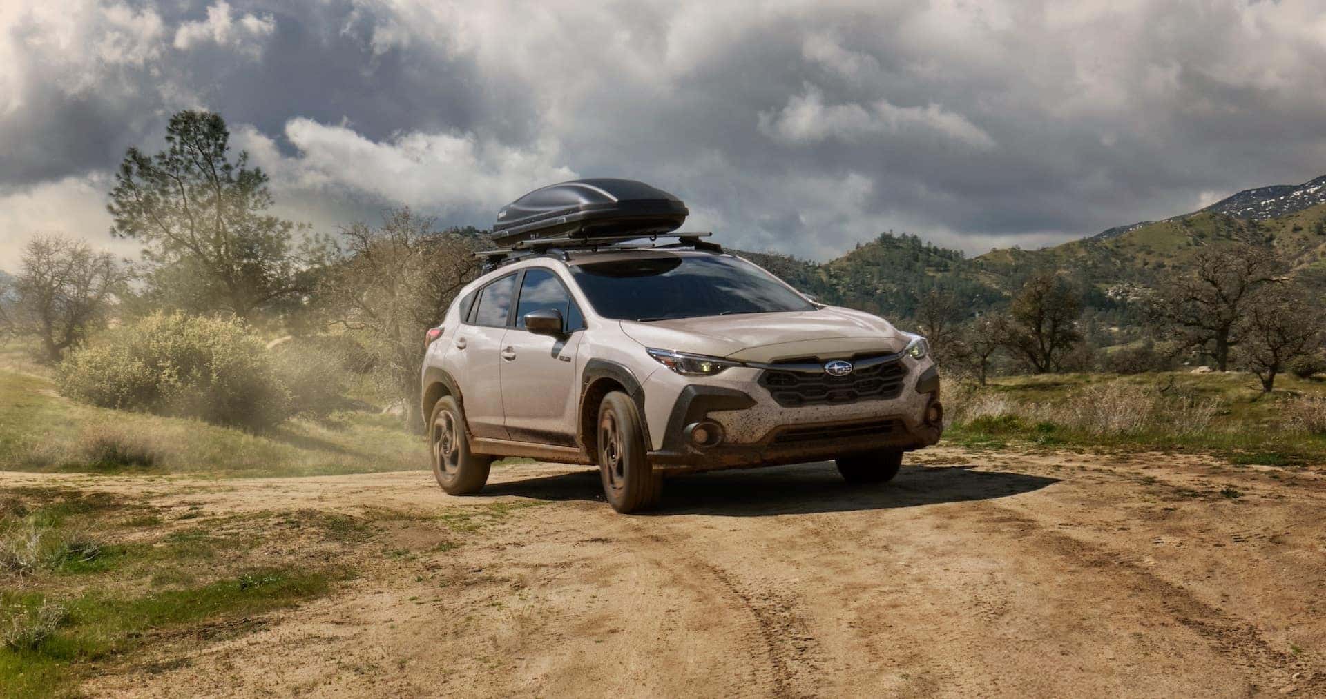 Tan Subaru Crosstrek with a roof box on a dirt road