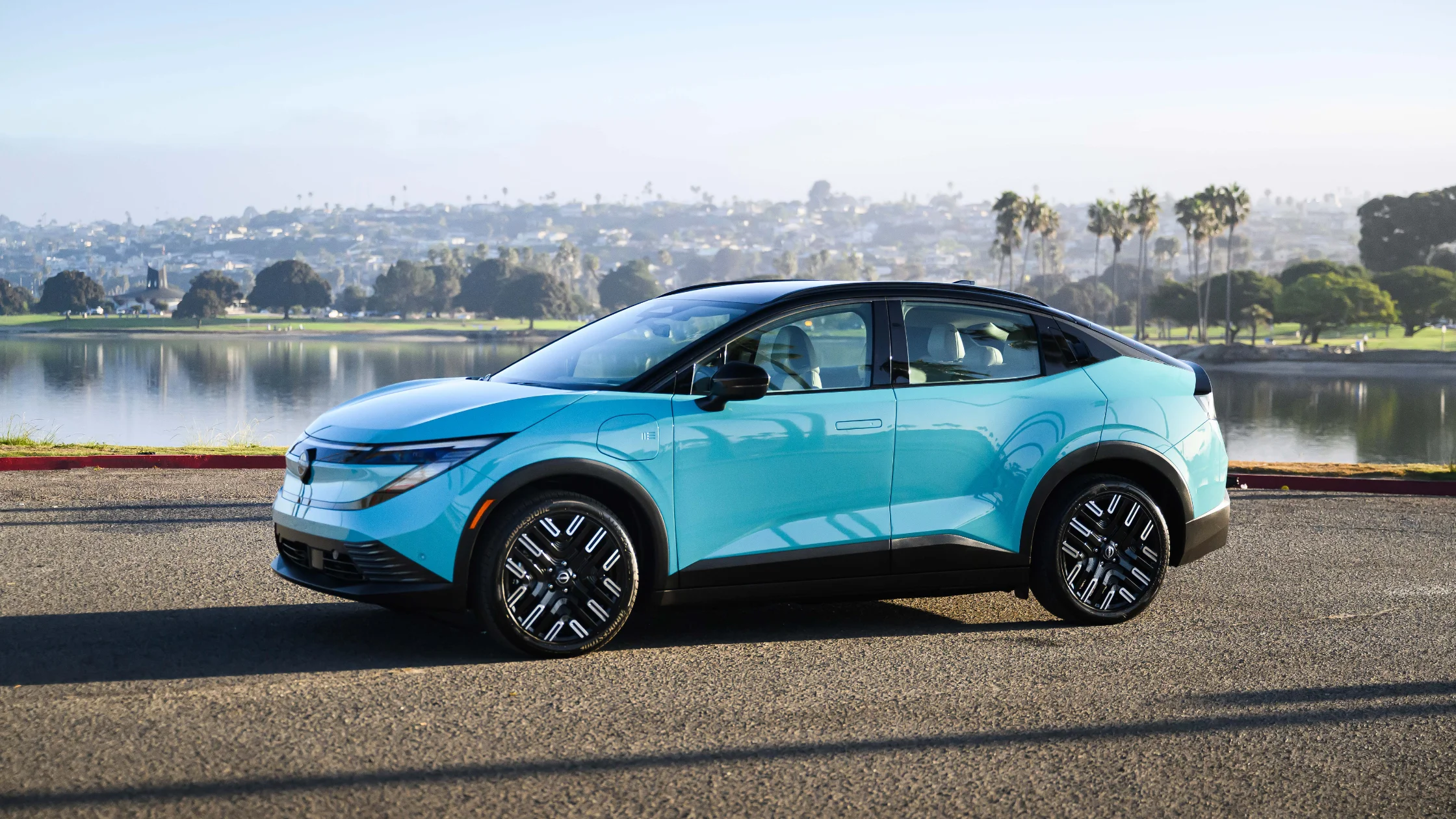 2026 Nissan LEAF® blue electric hatchback parked beside lake with palm trees in background