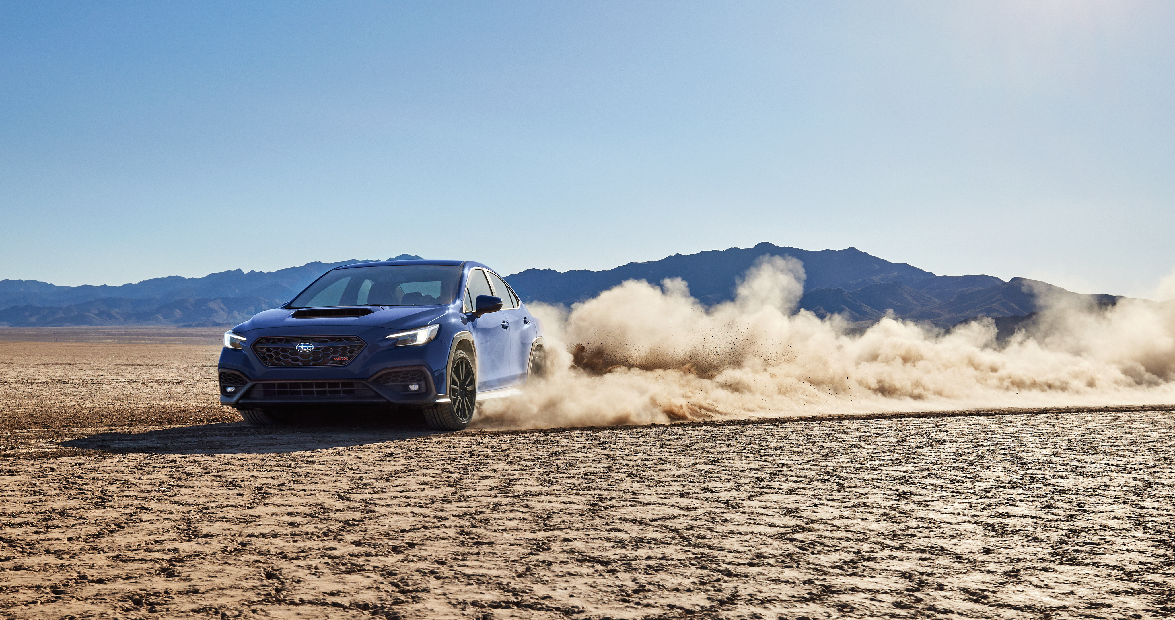 26_WRX_features_hero_gallery_1.png / A WRX high-performance sports sedan drifts a turn on a desert bed, kicking up a cloud of dust.