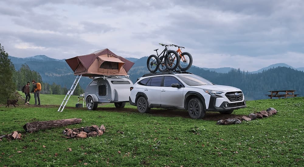 A white 2023 Subaru Outback parked with a small camper at a remote site.