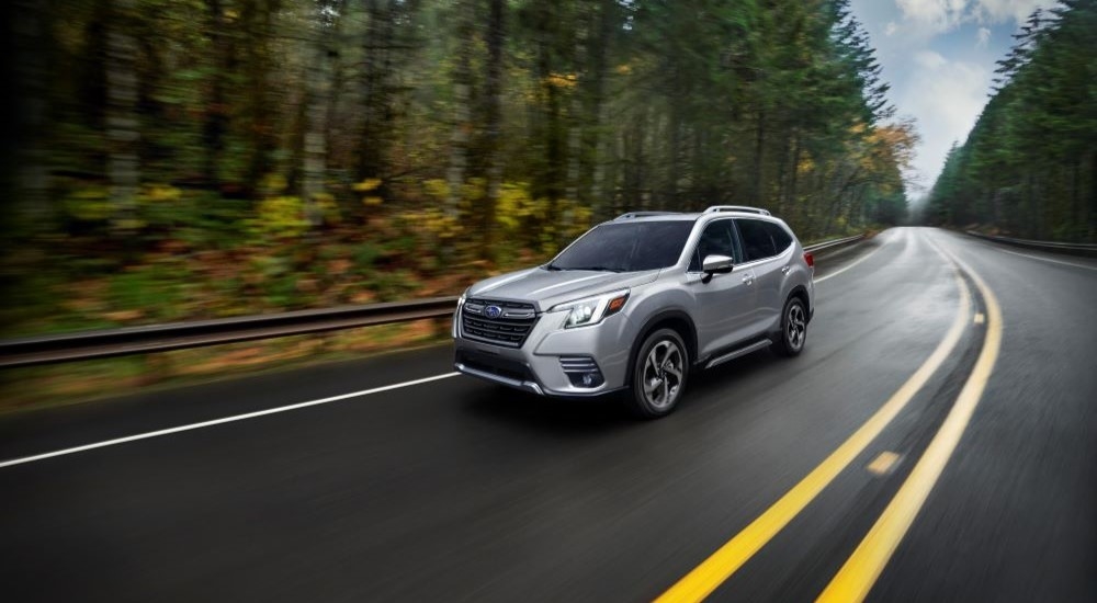 A silver 2023 Subaru Forester is shown driving on a tree-lined road