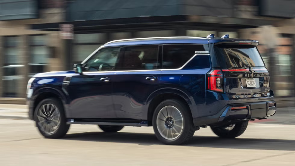 2027 Nissan Armada in dark blue driving on a city street, rear three-quarter view