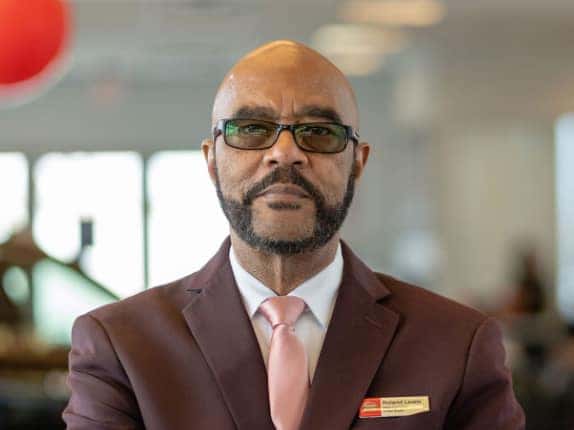 Roland Lewis, United Nissan team member, in a maroon suit and tinted glasses inside the dealership