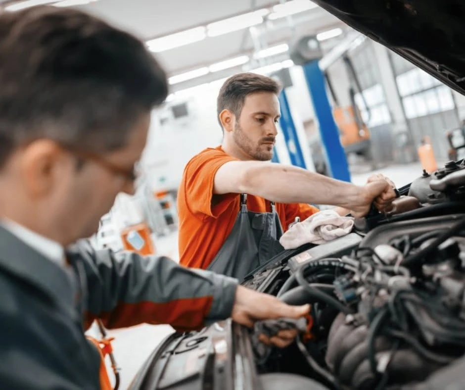 Two service technicians working on a vehicle engine in an auto repair bay