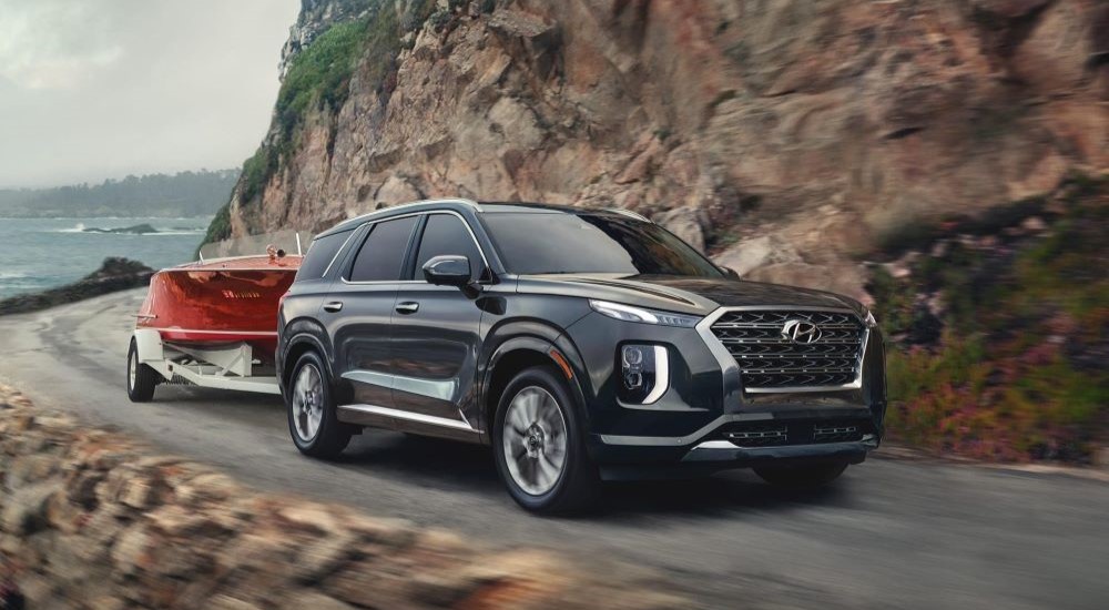 A black 2020 Hyundai Palisade is shown towing a small red boat on a winding road.