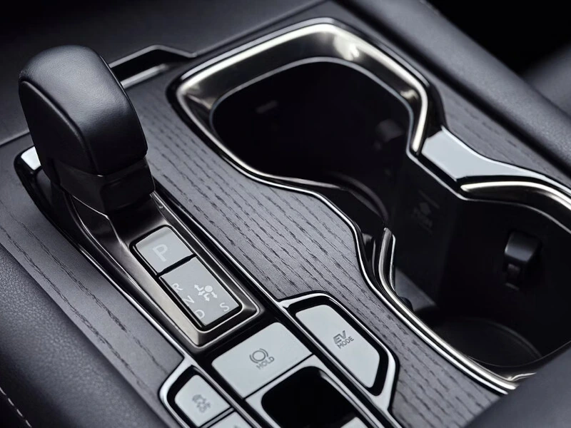 Close-up of a car's gear shift lever and cup holders on a sleek wooden console. Buttons for parking and driving modes are visible, conveying modernity.