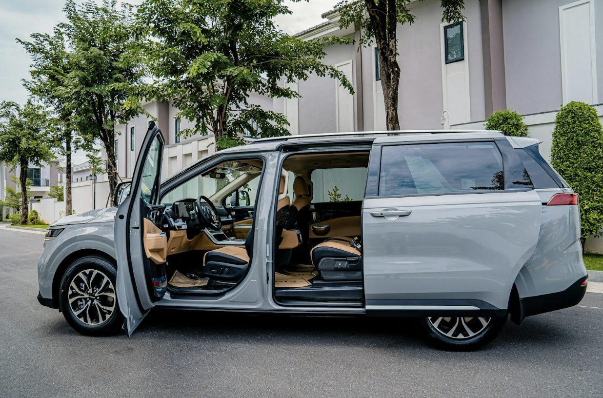 A modern gray minivan (MPV) with all doors open, revealing a luxurious tan interior, parked outdoors.