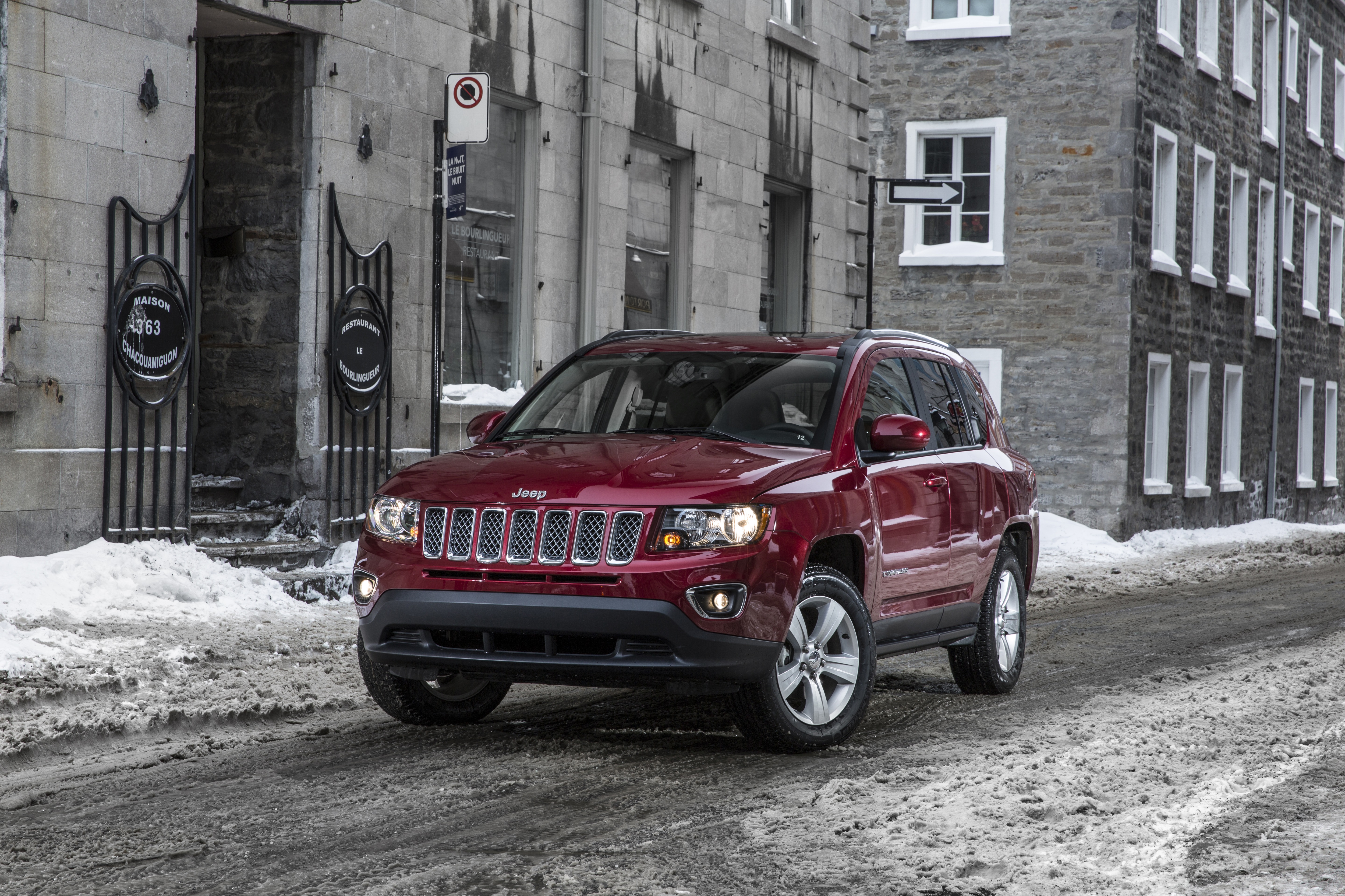 Red Jeep Compass driving on a snowy street lined with buildings