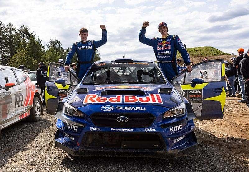 Rally drivers celebrating on top of their Subaru rally car