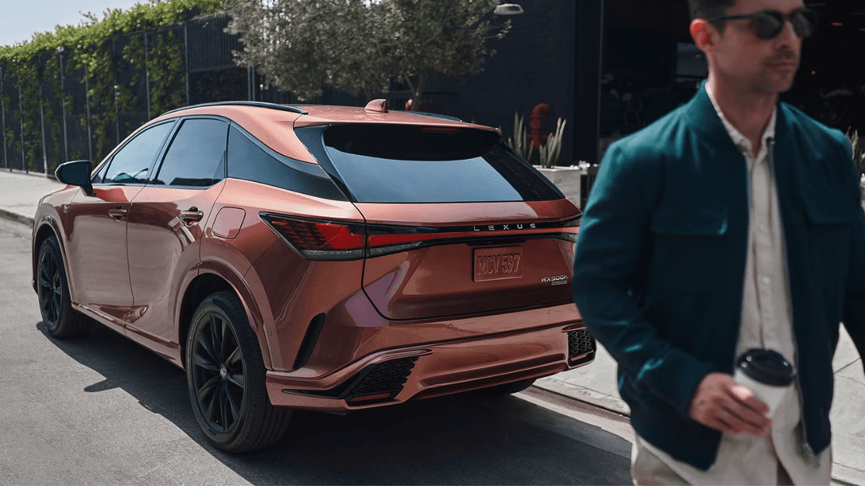 Rear view of the 2024 Lexus RX next to a person holding a coffee cup