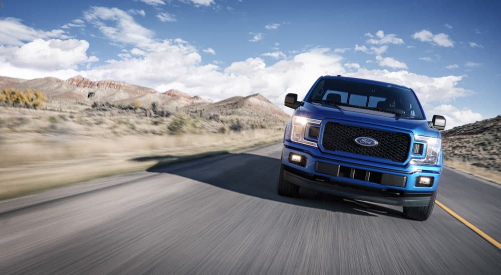 A blue 2018 Ford F-150 is shown driving on a highway after leaving a used car dealership.
