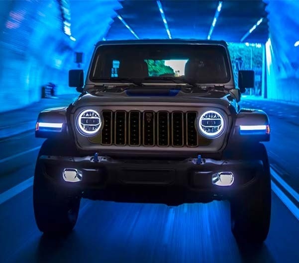 Front view of a Jeep Wrangler with glowing headlights in a blue-lit garage
