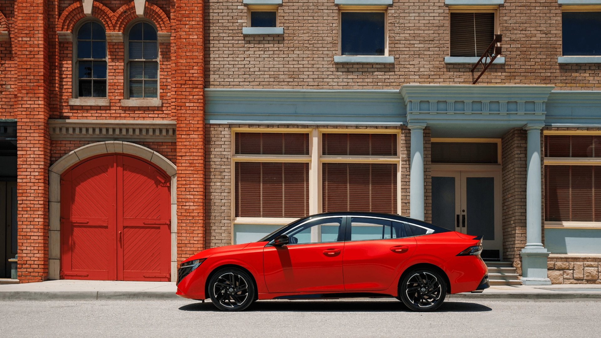 2025 Nissan Sentra® red sedan side profile parked on city street beside brick storefronts downtown