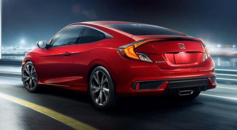 A red 2020 Honda Civic Coupe Sport is driving on a city street at night, facing away.