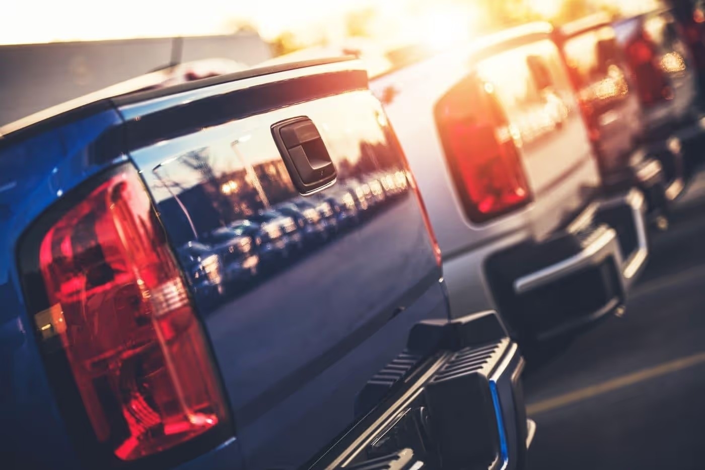 Row of pickup truck tailgates on a dealership lot at sunset
