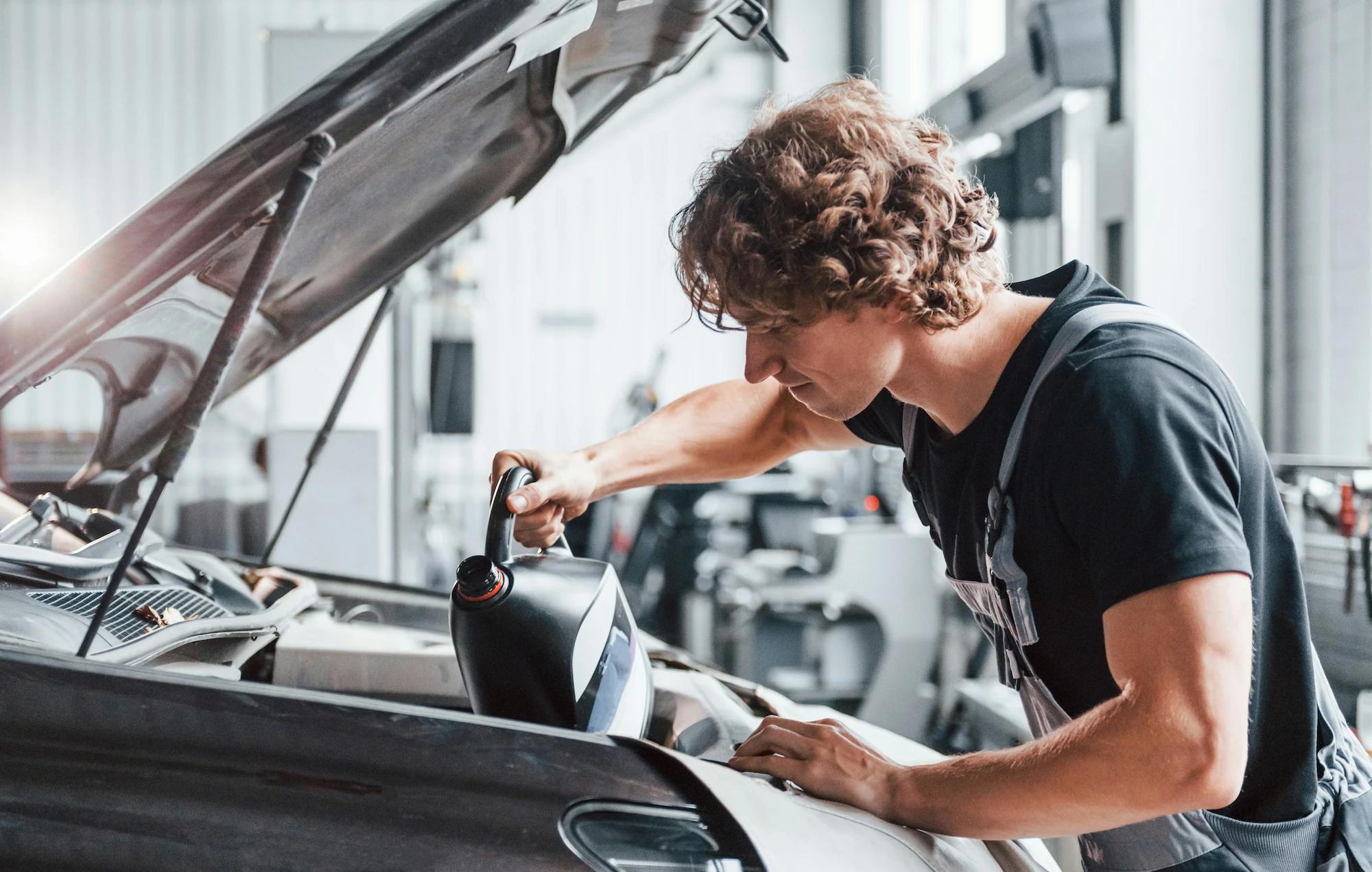 Technician pouring fluid into a vehicle's engine bay during a service appointment