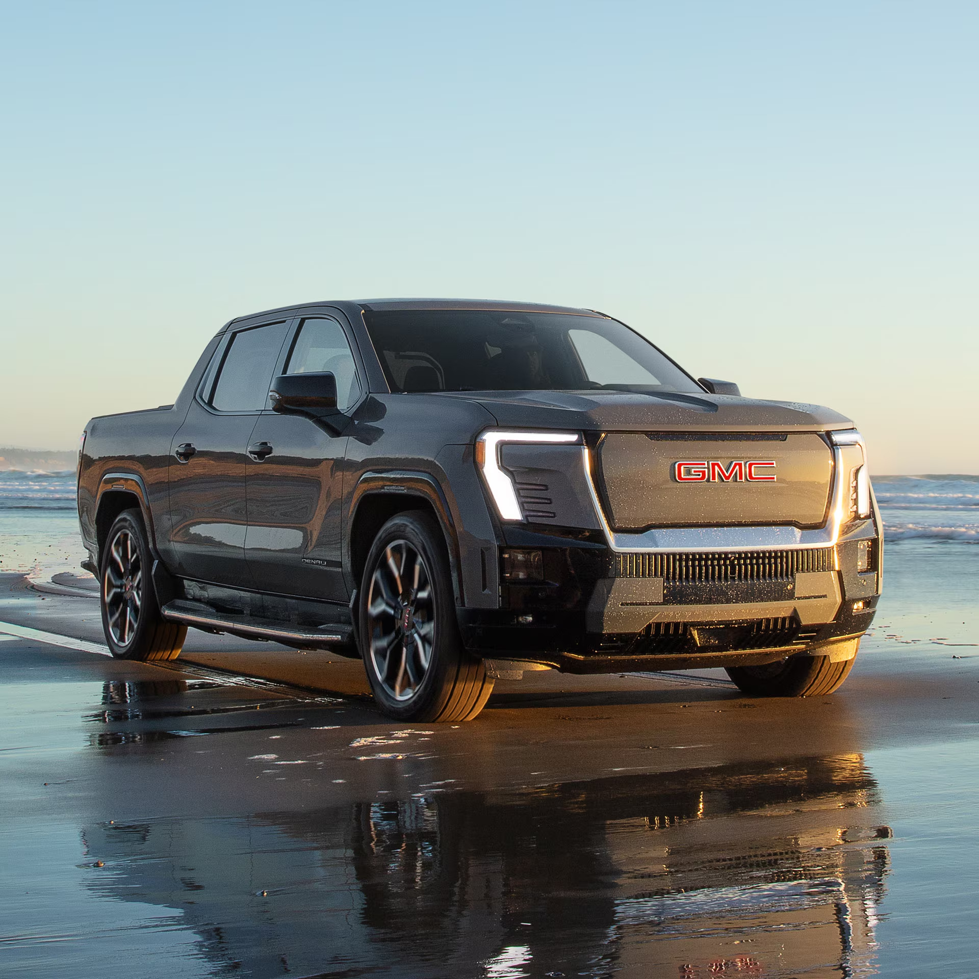 Dark gray GMC Sierra EV Denali on a wet beach at sunset