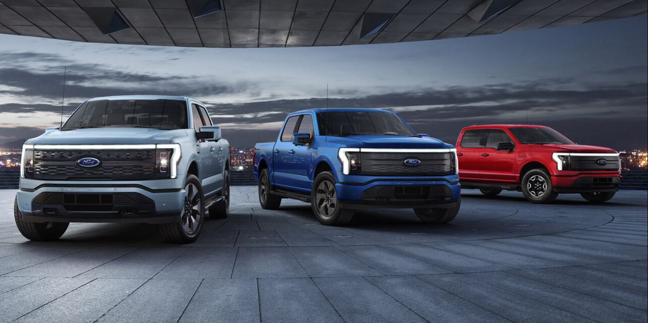 pictured left to right: white 2025 Ford Electric Truck, blue 2025 Ford Electric Truck, and a red 2025 Ford Electric Truck parked on a pavement runway