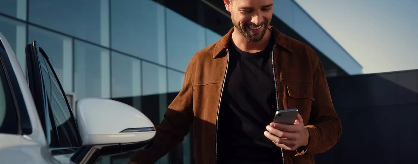 Man smiling at his phone next to a white 2026 Genesis G80